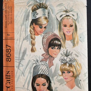 May include: Vintage McCall's sewing pattern for bridal caps and veils. The pattern includes two sizes: small (21 1/4 - 22 inches) and large (22 1/4 - 23 inches). The pattern shows five different styles of bridal headwear, including a white cap with a feather, a white bow, a brown cap with a veil, a white cap with a flower, and a white cap with a veil.
