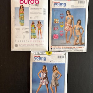 May include: Three Burda Young fashion sewing pattern packets. The packets feature images of women in swimwear and dresses. The packets include the pattern numbers 7228, 8038, and 7913. The packets are white with colorful images.
