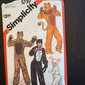 Puede incluir: Un sobre de patrón de costura Simplicity 5739 para disfraces de talla 6-8. El frente muestra ilustraciones de cuatro disfraces de animales: un oso marrón, un león amarillo, un gato negro con un lazo rosa y un conejo blanco, todos con capuchas y manoplas.