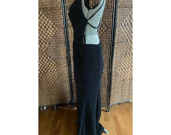 May include: A black, floor-length dress with a unique open back design. The dress features a fitted bodice with a plunging neckline and spaghetti straps. The skirt flows to the floor. The dress is displayed on a mannequin.