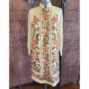 May include: A vintage yellow dress with long sleeves and a mandarin collar. The dress features a floral pattern in brown and orange, with vertical stripes. The dress is knee-length and has a button-down front.