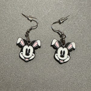 May include: A pair of silver earrings with black and white Mickey Mouse heads with pink bunny ears.