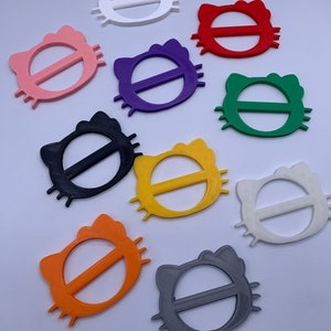 May include: Assortment of ten colorful plastic cat-shaped belt buckles. The buckles are in various colors, including white, pink, red, purple, green, black, yellow, orange, and gray.