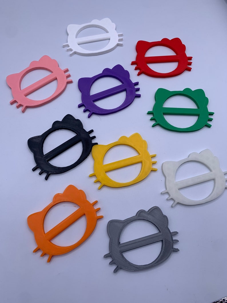 May include: Assortment of ten colorful plastic cat-shaped belt buckles. The buckles are in various colors, including white, pink, red, purple, green, black, yellow, orange, and gray.