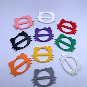 May include: Ten colorful plastic cat-shaped belt buckles in various colors including black, white, pink, red, purple, yellow, orange, green, and gray.