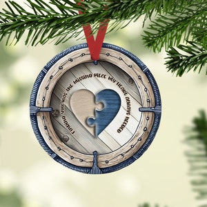 Peut inclure: Une décoration de Noël ronde en bois avec une bordure en corde bleue et blanche. L'ornement présente une pièce de puzzle en forme de cœur avec le texte "Finding you was the missing piece my heart always needed".