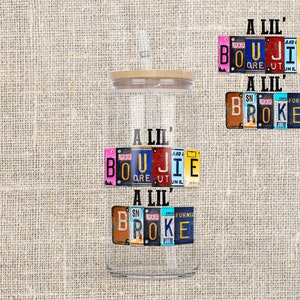 Op de afbeelding: Een doorzichtige glazen beker met een houten deksel en een ontwerp van kleurrijke kentekenplaten met de tekst "A Lil' Boujie A Lil' Broke".