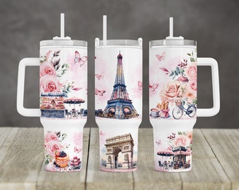 May include: White travel mugs with a handle and straw feature Parisian-themed designs. The designs include the Eiffel Tower, Arc de Triomphe, cafes, bicycles, pink roses, and butterflies. The mugs are decorated with watercolor illustrations.