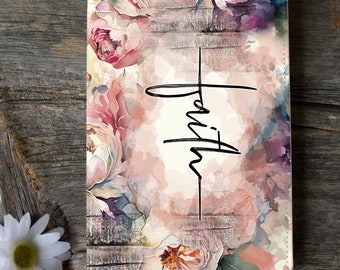 May include: A floral-themed journal with the word "Faith" in black script. The cover features a watercolor design of pink and purple flowers against a backdrop of weathered wood. The journal is rectangular and appears to be made of a leather-like material.