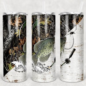 May include: A set of three stainless steel tumblers with a camouflage and birch bark design. The tumblers feature a black and white illustration of a fish with a fishing line and lure.