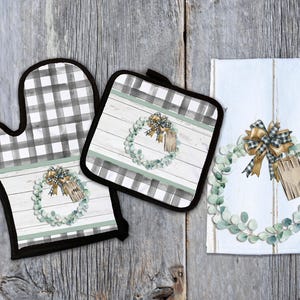 May include: A set of three kitchen items featuring a wreath design with a rustic wood background. The set includes a potholder, oven mitt, and a tea towel. All three items feature a black and white checkered pattern.