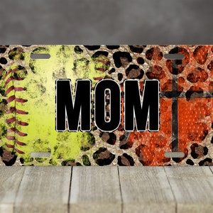 May include: A license plate with a leopard print background and a softball and basketball design. The word "MOM" is printed in black letters on the plate.