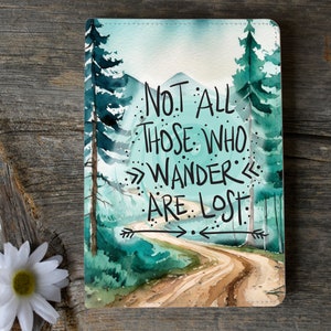 May include: A watercolor painting of a winding dirt road through a forest with the quote "Not all those who wander are lost" written in black.