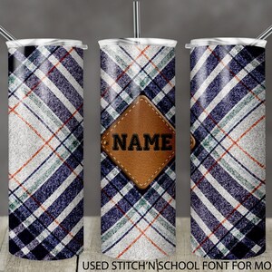 Może przedstawiać: Zestaw trzech kubków ze stali nierdzewnej z wzorem w kratę w kolorze niebieskim, białym i czerwonym. Środkowy kubek ma brązową skórzaną łatę z napisem "NAME" białymi literami.