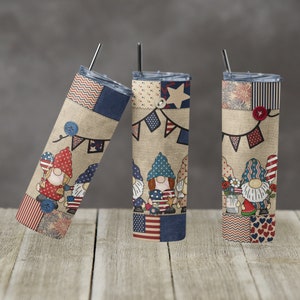 Könnte beinhalten: Drei patriotisch gestaltete Becher mit Edelstahlstrohhalmen. Jeder Becher hat ein Patchwork-Design mit Zwergen, amerikanischen Flaggen, Sternen und Wimpeln in Rot, Weiß und Blau. Die Becher sind für kalte Getränke konzipiert.