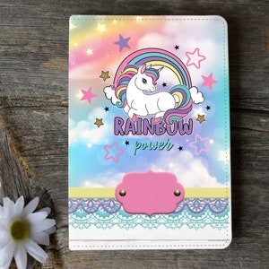 May include: A white notebook cover with a rainbow, a unicorn, and stars. The text "RAINBOW power" is printed on the cover.