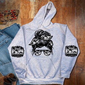 May include: A gray hooded sweatshirt with a black and white graphic of a woman with a messy bun and sunglasses. The graphic has a pattern of wrestlers in the hair and sunglasses. The sleeves have a patch with the word "Wrestling" and a pattern of wrestlers.