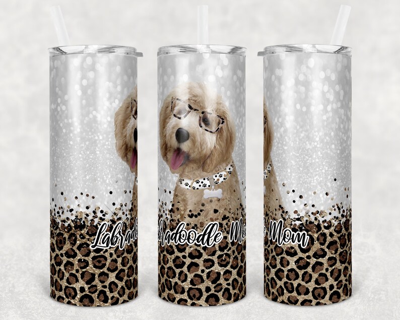May include: Three stainless steel tumblers with a glitter background and a leopard print design. The center tumbler features a doodle dog wearing glasses and a collar with a bone charm. The text "Doodle Mom" is printed on the tumbler. The left tumbler has the text "Labradoodle" and the right tumbler has the text "Mom".