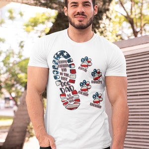 Könnte beinhalten: Weißes T-Shirt mit einem rot-weiß-blauen amerikanischen Flaggen-Design eines Fußabdrucks mit den Worten "Happy Father's Day to the Best Dog Dad" und Pfotenabdrücken mit den Namen "Caliber", "Brecher", "Barrett", "Colin" und "Lexi" darauf gedruckt.