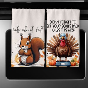 May include: Two kitchen towels with a fall theme. One towel features a squirrel with the text "nuts about fall". The other towel features a turkey with the text "Don't forget to set your scales back 10 lbs this week".