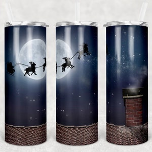 Puede incluir: Tres vasos de acero inoxidable con temática navideña. Los vasos presentan un cielo nocturno azul con luna llena, estrellas y Papá Noel volando en un trineo tirado por renos. El vaso del medio muestra a Papá Noel volando sobre un tejado con una chimenea. Los vasos tienen un fondo marrón texturizado.