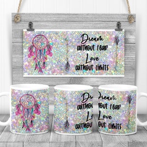 May include: Two white ceramic mugs with a pink and blue dreamcatcher design and glitter background. The mugs have the text "Dream without fear Love without limits" on them.