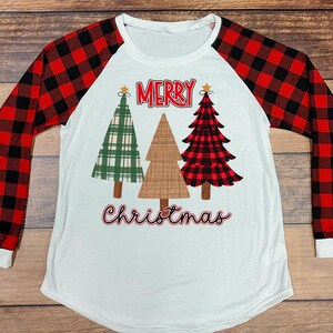 May include: White long-sleeved Christmas shirt with red and black buffalo plaid sleeves. The front features three Christmas trees and the words "MERRY Christmas" in red and black script.