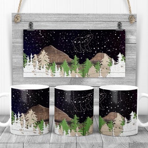 May include: Three white ceramic mugs with a design of a dark blue night sky with stars, a brown mountain, and a white outline of a bear constellation. The mugs are on a light wood surface.