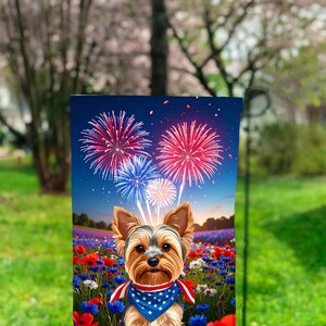 Peut inclure: Un drapeau de jardin avec un Yorkshire Terrier portant un bandana patriotique, sur fond de fleurs rouges, blanches et bleues. Des feux d'artifice éclatent dans le ciel nocturne au-dessus du chien, créant une scène festive.