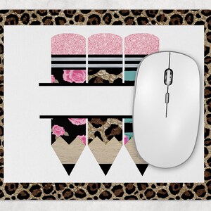 May include: A white mousepad with a leopard print border. The center of the mousepad features a design of three pencils with a pink glitter top, black and white stripes, and floral accents. The pencils are arranged vertically.