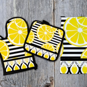 May include: A set of three kitchen accessories featuring a black and white striped pattern with yellow lemon slices. The set includes a potholder, an oven mitt, and a kitchen towel.