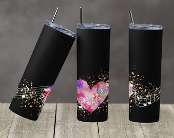 Puede incluir: Tres vasos de acero inoxidable negro con tapas y pajitas. Los vasos presentan un corazón de acuarela con notas musicales y purpurina dorada sobre un fondo negro.