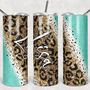 Pode incluir: Três copos de aço inoxidável com um design de glitter turquesa e dourado. Os copos têm um padrão de estampa de leopardo preto e dourado e a palavra "Irmã" está escrita em branco no copo do meio.