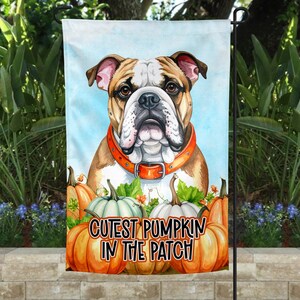 Op de afbeelding: Tuinvlag met een illustratie van een bulldog met een oranje halsband. De vlag heeft de tekst "Cutest Pumpkin in the Patch" met pompoenen op de voorgrond. De achtergrond is een lichtblauwe lucht.