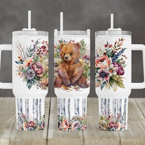 May include: Three white stainless steel tumblers with a brown bear and floral design. The tumblers have a handle and a straw.