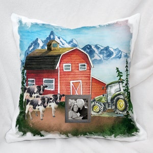 May include: A watercolor painting of a red barn with a black roof, a green tractor, and three black and white cows in front of a mountain range. A framed photo of a couple is in the foreground.