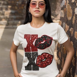 May include: White t-shirt with a red and black glitter design of the letters "XO" with two red and black glitter lips.