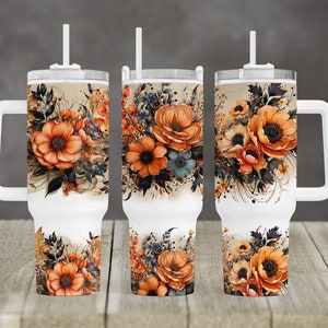 Puede incluir: Tres vasos de acero inoxidable blanco con tapas y pajitas. Cada vaso presenta un diseño floral diferente con flores naranjas, marrones y azules sobre un fondo beige.