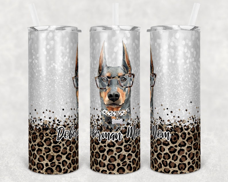 May include: Three stainless steel tumblers with a silver glitter background and a leopard print design. The tumblers feature a Doberman Pinscher wearing glasses and a bow tie. The text "Doberman Mom" is printed on the tumblers.