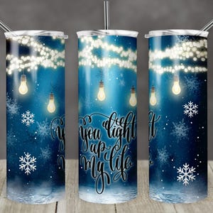 May include: A blue and white tumbler with a design of string lights and snowflakes. The text "You light up my life" is written on the tumbler.