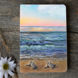 May include: Two baby sea turtles crawl on a sandy beach towards the ocean. The ocean is blue and green with waves crashing on the shore. The sky is a soft pink and orange with a few white clouds.