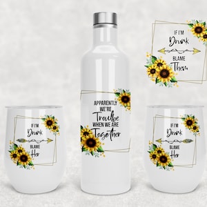 May include: White drinkware set featuring sunflower designs and humorous text. Includes a water bottle, two stemless wine glasses, and a decorative label. The text reads "If I'm Drunk Blame Her", "If I'm Drunk Blame Them", and "Apparently We're Trouble When We Are Together."