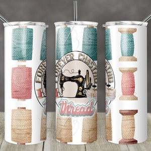 Puede incluir: Un vaso blanco con temática de costura. Presenta una máquina de coser vintage, carretes de hilo y el texto "Forever Chasing Thread".