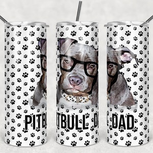 Pode incluir: Um copo de aço inoxidável branco com um padrão de pegadas de patas pretas e o texto "Pitbull Dad" na frente. O copo tem uma tampa preta e um canudo transparente.