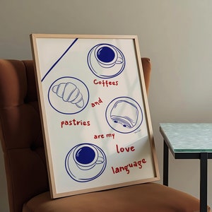 May include: A white framed print with blue and red text that reads "Coffees and pastries are my love language". The print features illustrations of a croissant, a pastry, a cup of coffee, and a toaster.