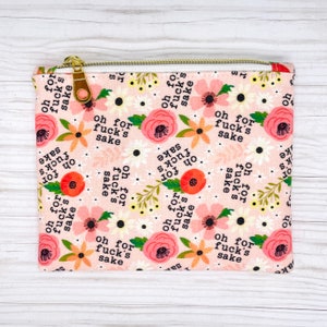 Puede incluir: Una bolsa de tela rosa con cierre de cremallera. La bolsa est&aacute; decorada con un patr&oacute;n floral y la frase "oh for fuck's sake" repetida en todo.