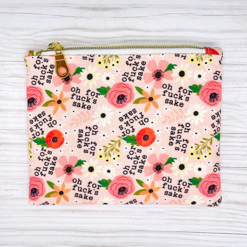 Puede incluir: Una bolsa de tela rosa con cierre de cremallera. La bolsa est&aacute; decorada con un patr&oacute;n floral y la frase "oh for fuck's sake" repetida en todo.