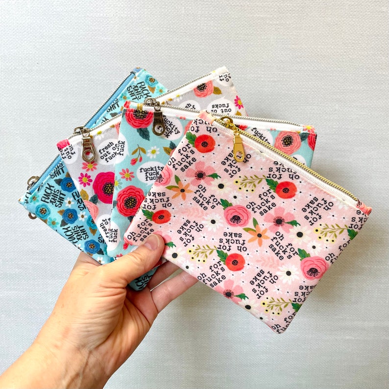 Puede incluir: Cinco peque&ntilde;as bolsas con cremallera con estampado floral y la frase "oh for fuck's sake" repetida en cada bolsa. Las bolsas son de varios tonos de azul y rosa.
