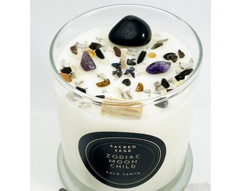 Puede incluir: Una vela blanca con una etiqueta negra que dice "Sacred Sage Zodiac Moon Child Palo Santo". La vela está cubierta con varios cristales y piedras, incluyendo amatista, obsidiana negra y ojo de tigre.