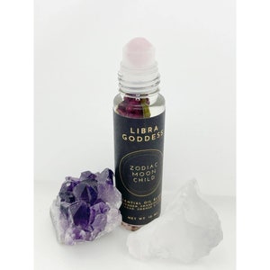 May include: A glass roller bottle with a pink roller ball and a black label that says "LIBRA GODDESS ZODIAC MOON CHILD ESSENTIAL OIL BLEND LAVENDER, FRANKINCENSE, CEDAR, ORANGE & YLANG YLANG NET WT. 10 ML"